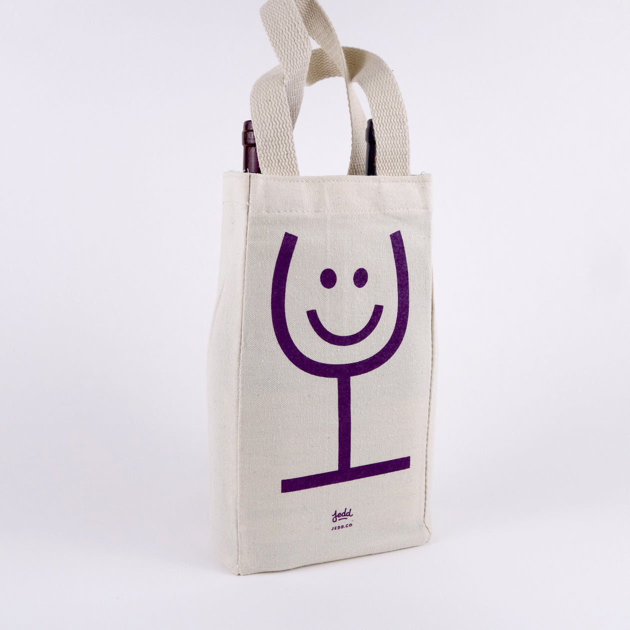 A canvas wine tote with a glass of wine smiley face illustration screen printed in purple.