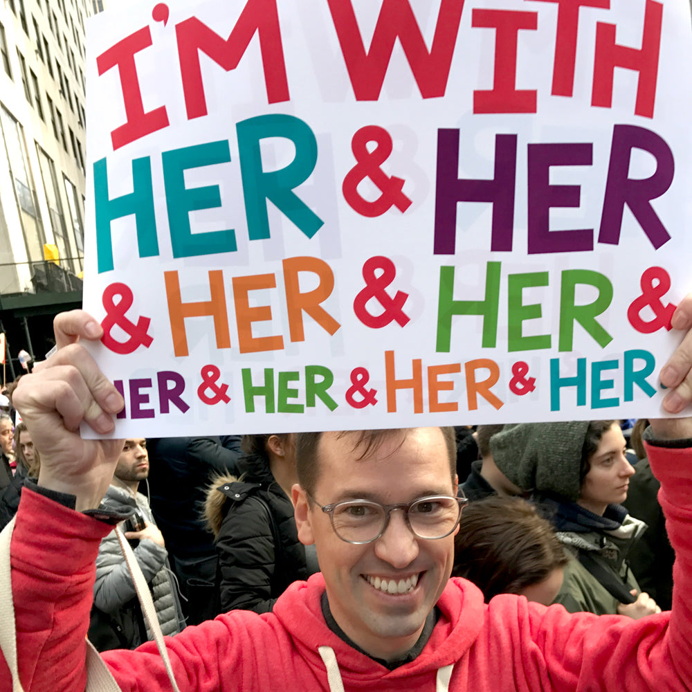 A portrait of Jedd holding a sign reading "I'm With Her & Her & Her & Her & Her & Her & Her & Her & Her...